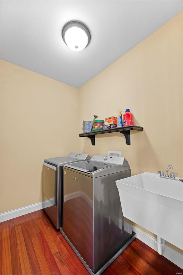 clothes washing area featuring washing machine and dryer, a sink, wood finished floors, laundry area, and baseboards