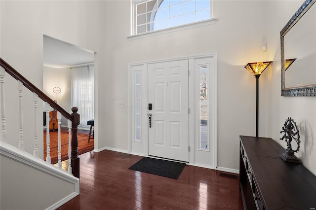 foyer entrance featuring visible vents, dark wood-style floors, baseboards, a towering ceiling, and stairs