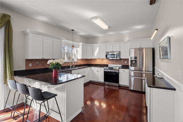 kitchen with pendant lighting, dark wood-style floors, appliances with stainless steel finishes, a peninsula, and white cabinets