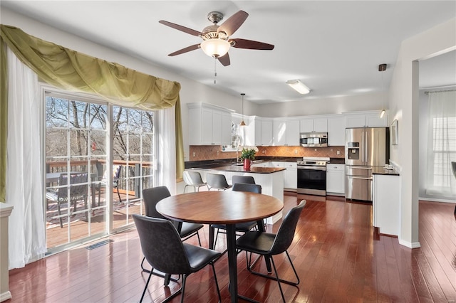 dining space with dark wood-type flooring, a ceiling fan, visible vents, and baseboards