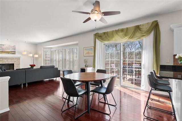 dining room with dark wood-style floors, a fireplace, and a ceiling fan