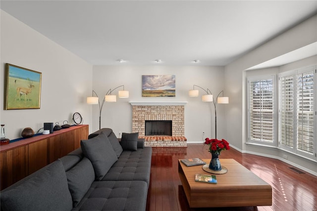 living area with a brick fireplace, visible vents, wood-type flooring, and baseboards