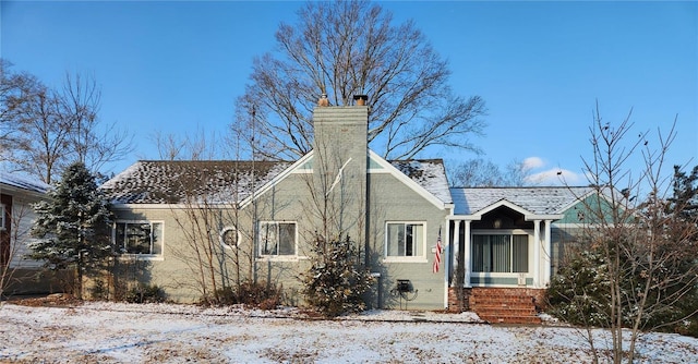 snow covered property with brick siding and a chimney