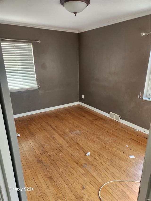 empty room featuring ornamental molding, wood finished floors, visible vents, and baseboards