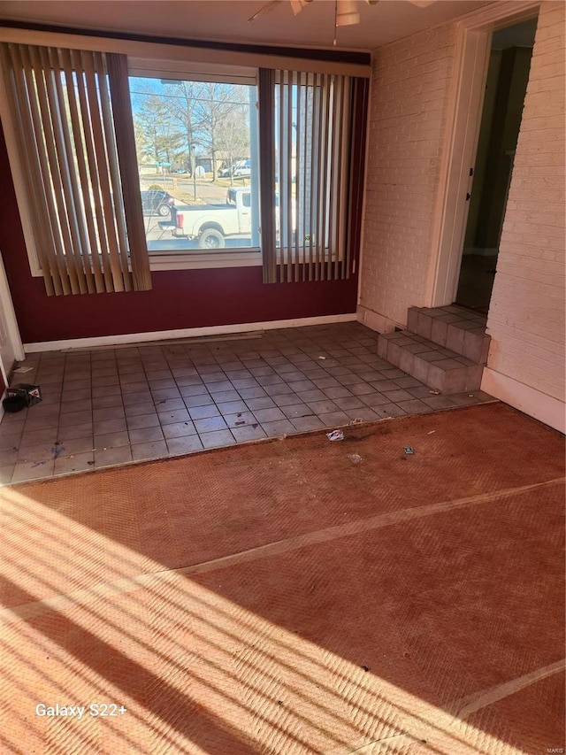 tiled empty room featuring brick wall and baseboards