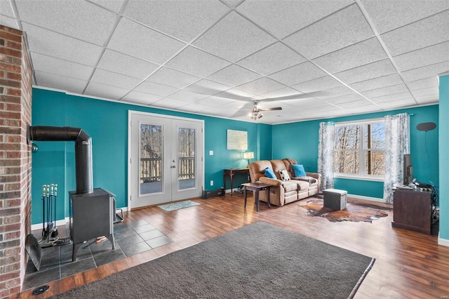 living room featuring ceiling fan, dark hardwood / wood-style floors, a drop ceiling, french doors, and a wood stove