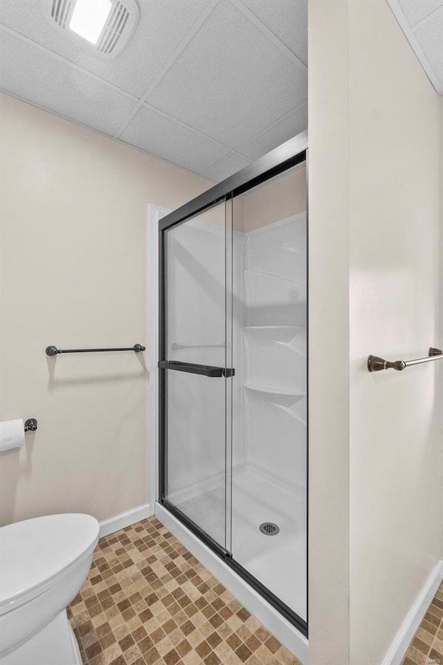 bathroom with a shower with door, a paneled ceiling, and toilet