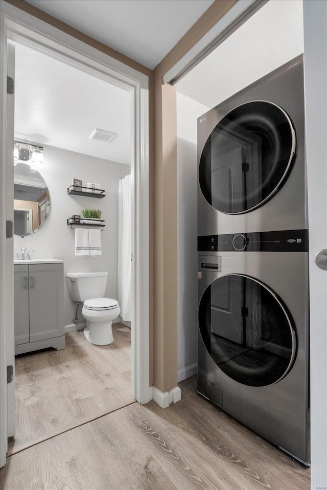 washroom with stacked washer / drying machine, sink, and light wood-type flooring