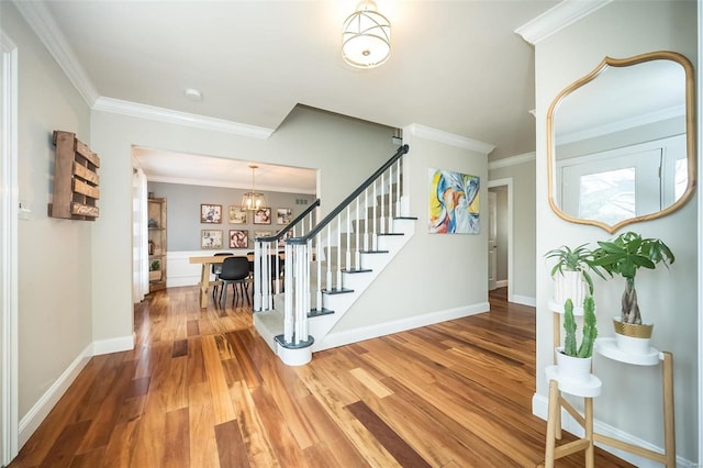 foyer featuring stairway, an inviting chandelier, ornamental molding, wood finished floors, and baseboards