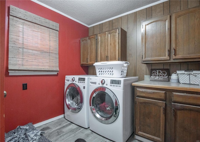 clothes washing area featuring washing machine and clothes dryer, cabinets, a textured ceiling, ornamental molding, and light hardwood / wood-style floors