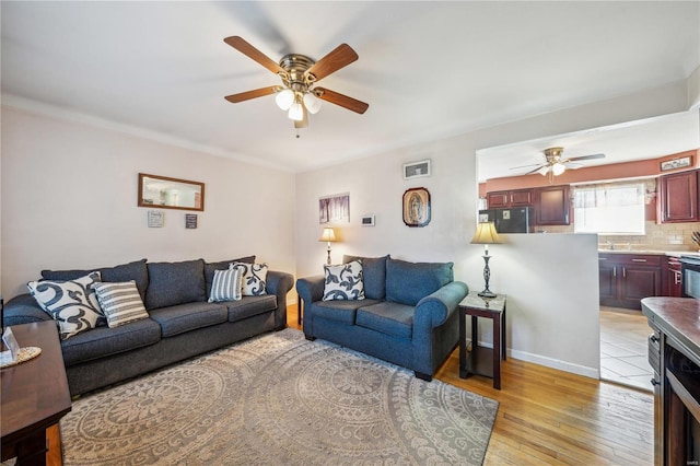 living room with light wood-style floors, visible vents, baseboards, and a ceiling fan