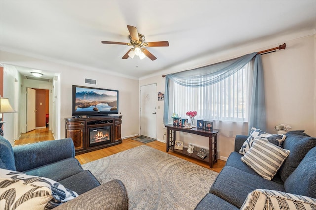 living area with visible vents, baseboards, a ceiling fan, light wood-type flooring, and a glass covered fireplace