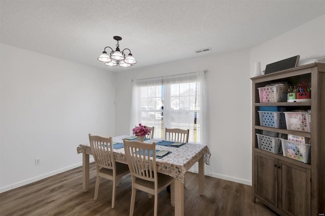 dining space with a textured ceiling, dark wood-style flooring, visible vents, baseboards, and an inviting chandelier