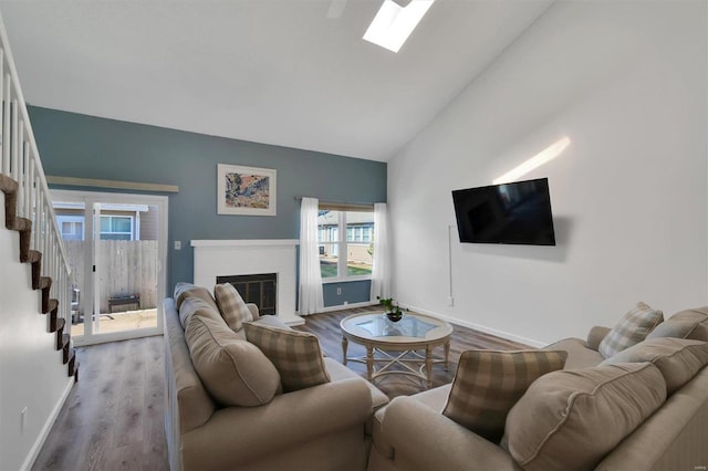 living room featuring a fireplace, wood finished floors, high vaulted ceiling, baseboards, and stairs