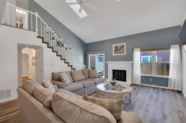 living area with ceiling fan, wood finished floors, visible vents, stairs, and a brick fireplace