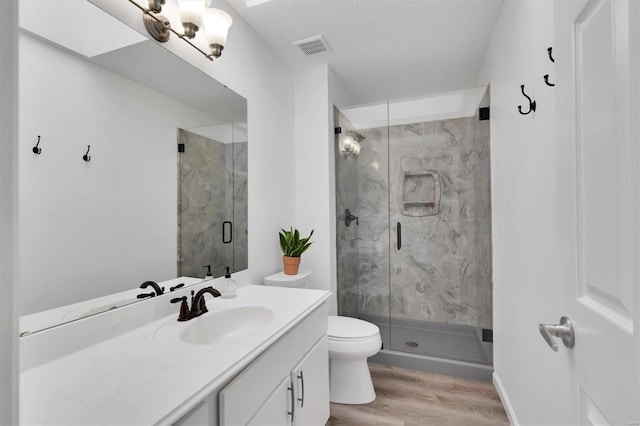 full bathroom with a marble finish shower, visible vents, toilet, vanity, and wood finished floors