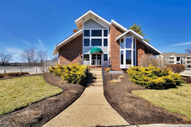 view of front facade with a front lawn, a chimney, fence, and brick siding