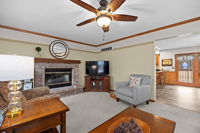 living area with visible vents, a fireplace, ornamental molding, ceiling fan, and carpet flooring