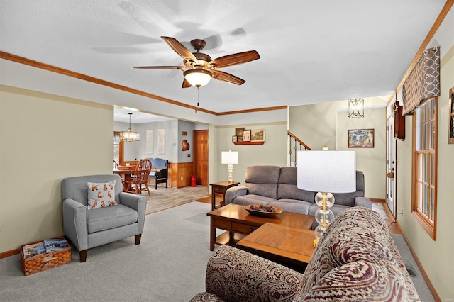 living room featuring light carpet, crown molding, stairs, and ceiling fan with notable chandelier