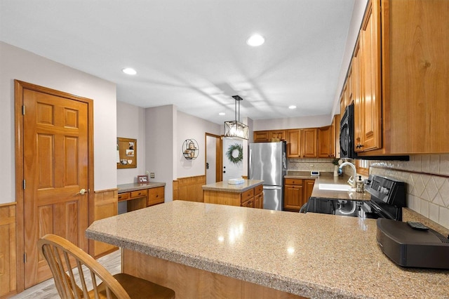 kitchen featuring a peninsula, brown cabinetry, wainscoting, and stainless steel appliances