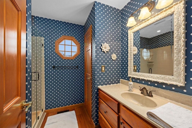 full bathroom with a shower stall, wallpapered walls, vanity, and wood finished floors