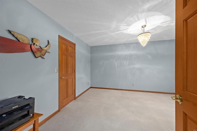 unfurnished room with light carpet, an inviting chandelier, a textured ceiling, and baseboards