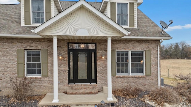 view of exterior entry with brick siding and roof with shingles