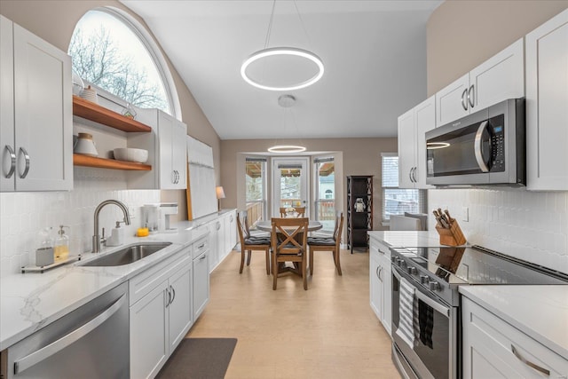 kitchen featuring light stone countertops, vaulted ceiling, stainless steel appliances, open shelves, and a sink