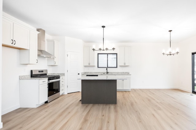 kitchen with a notable chandelier, stainless steel gas range oven, white cabinets, and wall chimney exhaust hood