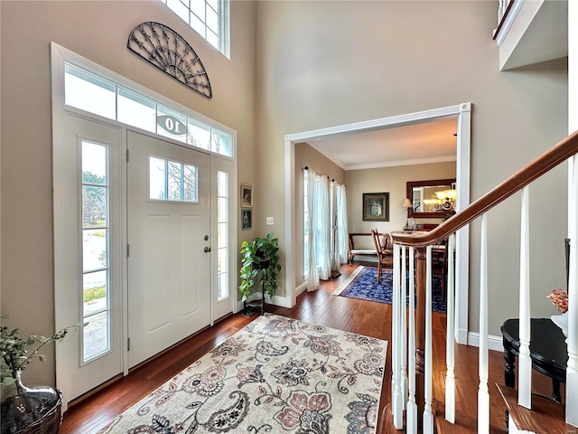 foyer featuring baseboards, stairway, ornamental molding, wood finished floors, and a high ceiling