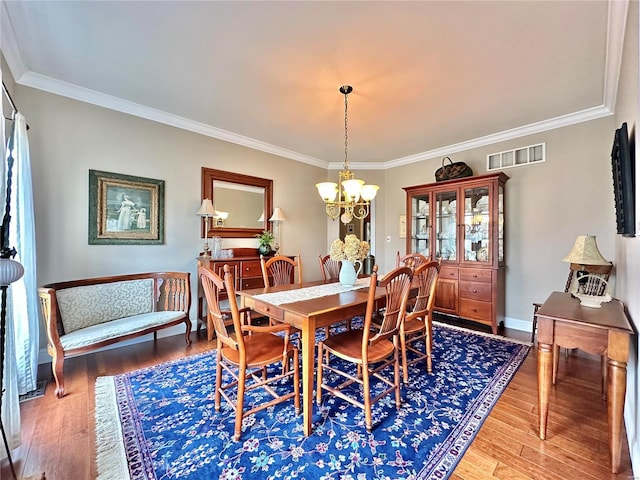 dining room featuring baseboards, visible vents, ornamental molding, wood finished floors, and a notable chandelier