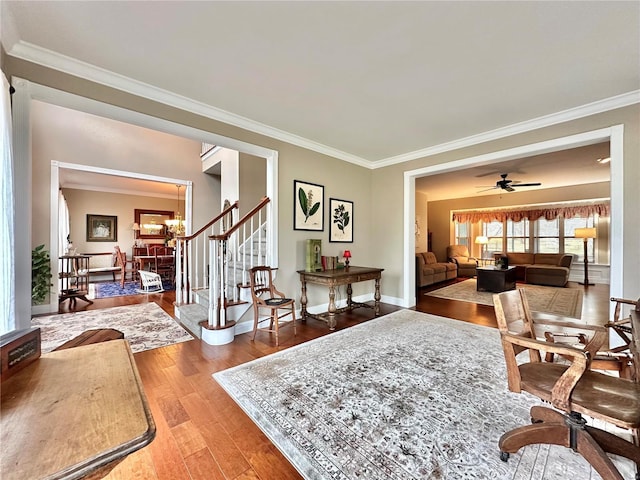 living room featuring ceiling fan with notable chandelier, baseboards, stairs, ornamental molding, and hardwood / wood-style floors