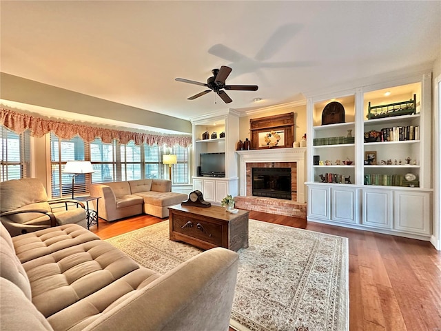 living area featuring ceiling fan, built in shelves, a brick fireplace, and wood finished floors