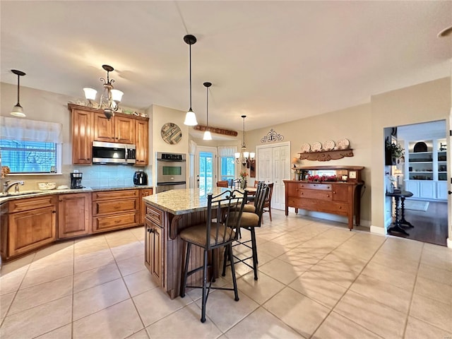 kitchen with a kitchen breakfast bar, appliances with stainless steel finishes, backsplash, brown cabinets, and an inviting chandelier