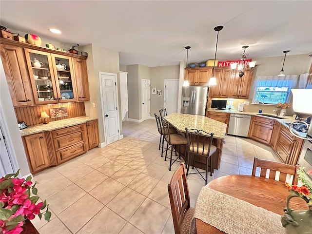 kitchen with light tile patterned floors, light stone counters, stainless steel appliances, a breakfast bar, and brown cabinetry