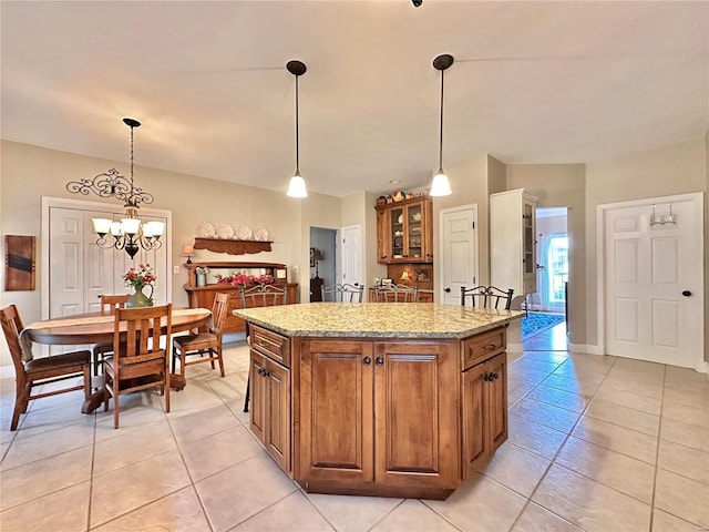 kitchen with pendant lighting, brown cabinetry, a center island, and light stone countertops