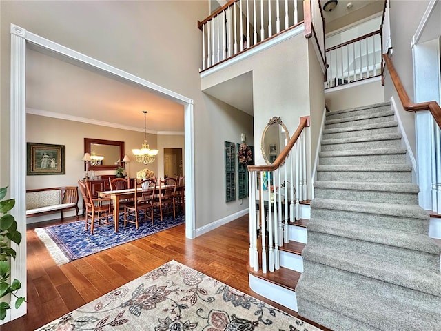 stairway with a notable chandelier, crown molding, a towering ceiling, wood finished floors, and baseboards