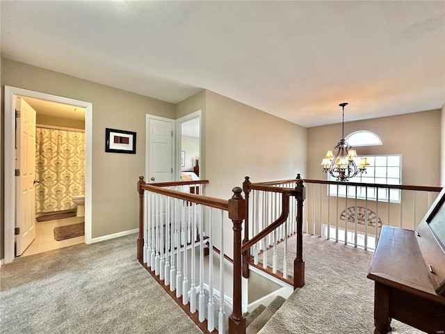 hallway featuring carpet floors, a chandelier, baseboards, and an upstairs landing