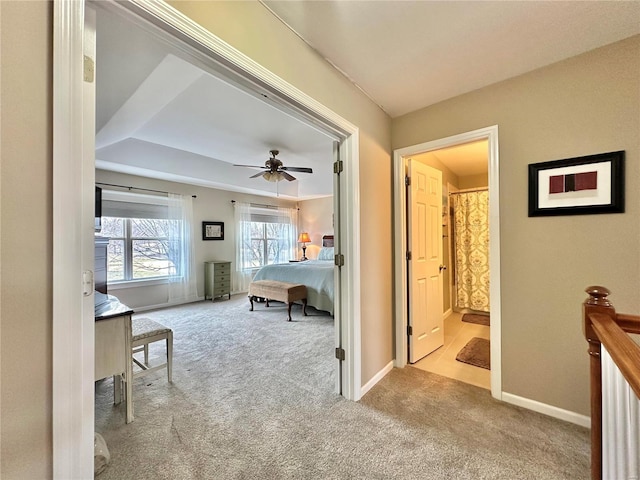 bedroom featuring a tray ceiling, carpet flooring, connected bathroom, ceiling fan, and baseboards