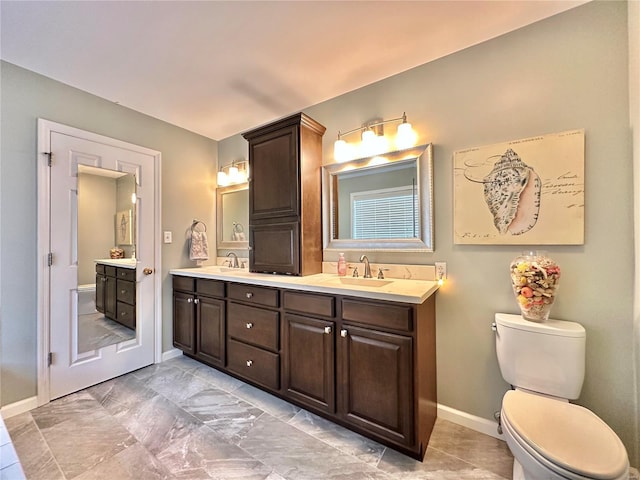 bathroom featuring baseboards, a sink, toilet, and double vanity