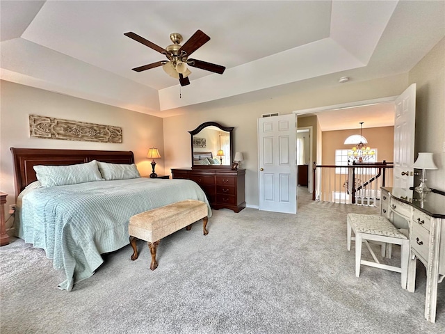 bedroom with light carpet, baseboards, a tray ceiling, and ceiling fan with notable chandelier