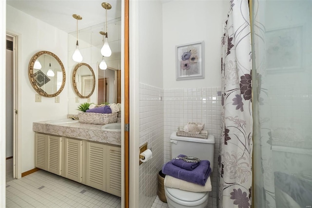 full bath with tile patterned floors, toilet, a sink, tile walls, and double vanity