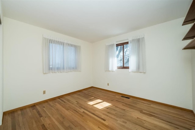 empty room with wood finished floors, visible vents, and baseboards