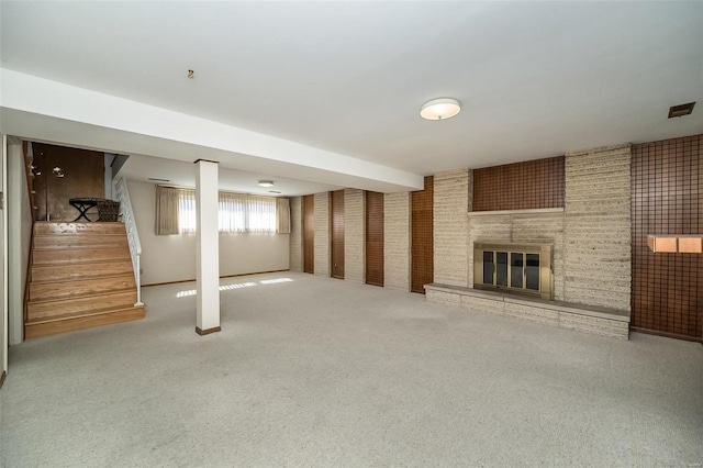 basement with carpet flooring, a brick fireplace, brick wall, and stairs