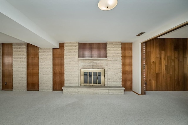 unfurnished living room with visible vents, carpet flooring, a fireplace, and wood walls