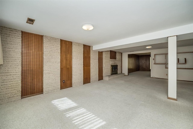 finished basement with carpet flooring, a fireplace, and brick wall