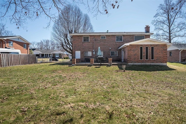 back of property with a yard, brick siding, a chimney, and fence