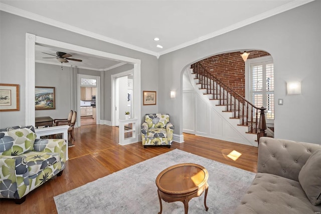 living room with crown molding, baseboards, stairs, wood finished floors, and arched walkways