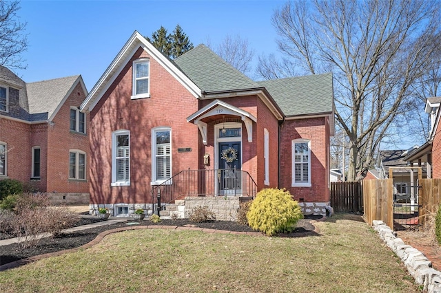 view of front facade with brick siding, a shingled roof, a front yard, and fence