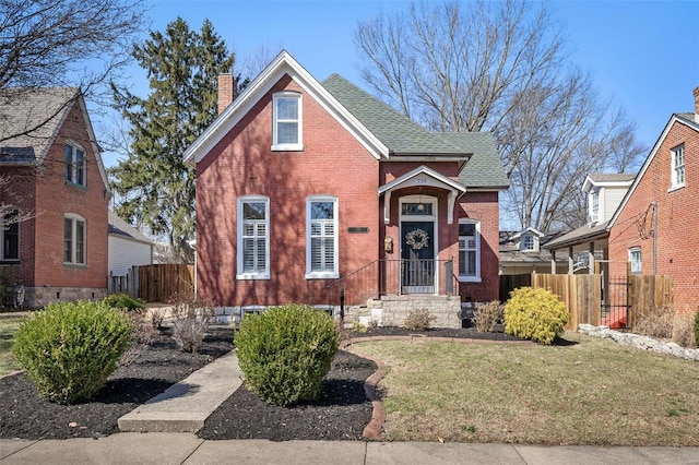 view of front of home featuring fence, roof with shingles, a front yard, brick siding, and a chimney